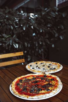 Delicious Italian pizzas topped with olives served on a rustic wooden table in an inviting indoor setting.