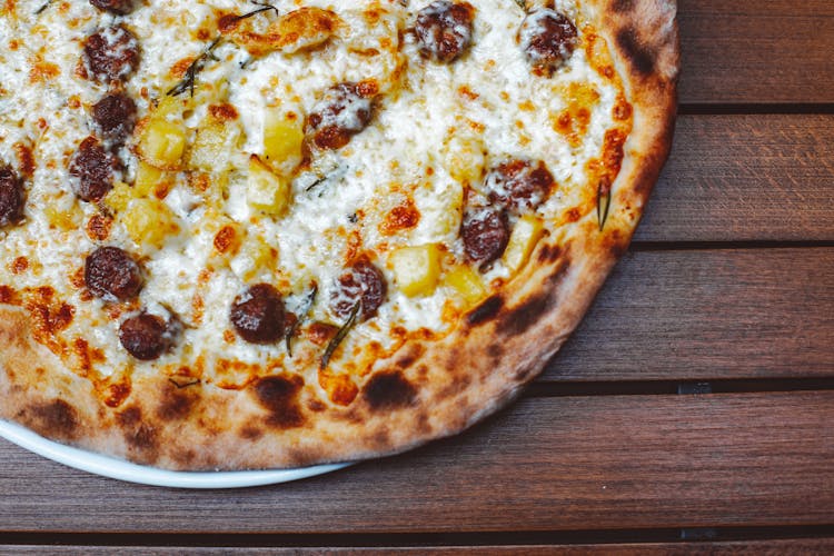 A Pizza With Cheese Toppings On A Wooden Table