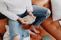 特写镜头：一个人坐在家里的皮沙发上，手里拿着现金数着