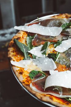 Close-up of a gourmet Italian pizza with prosciutto, parmesan, and arugula.
