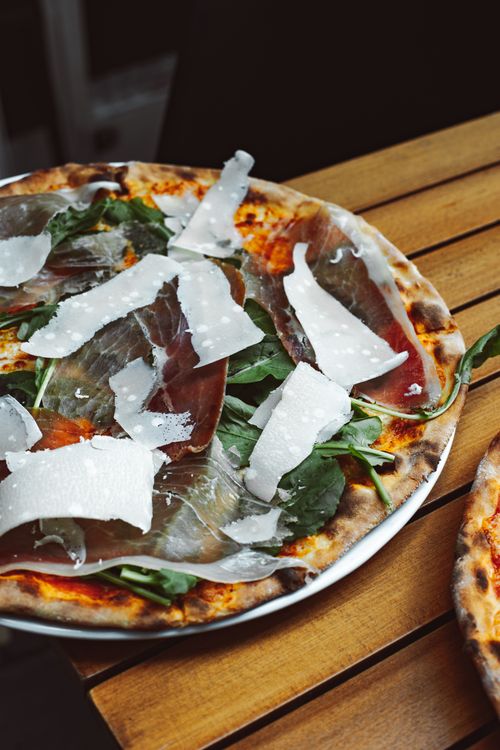 Free Delicious prosciutto and parmesan pizza on a rustic wood table, perfect for food lovers. Stock Photo