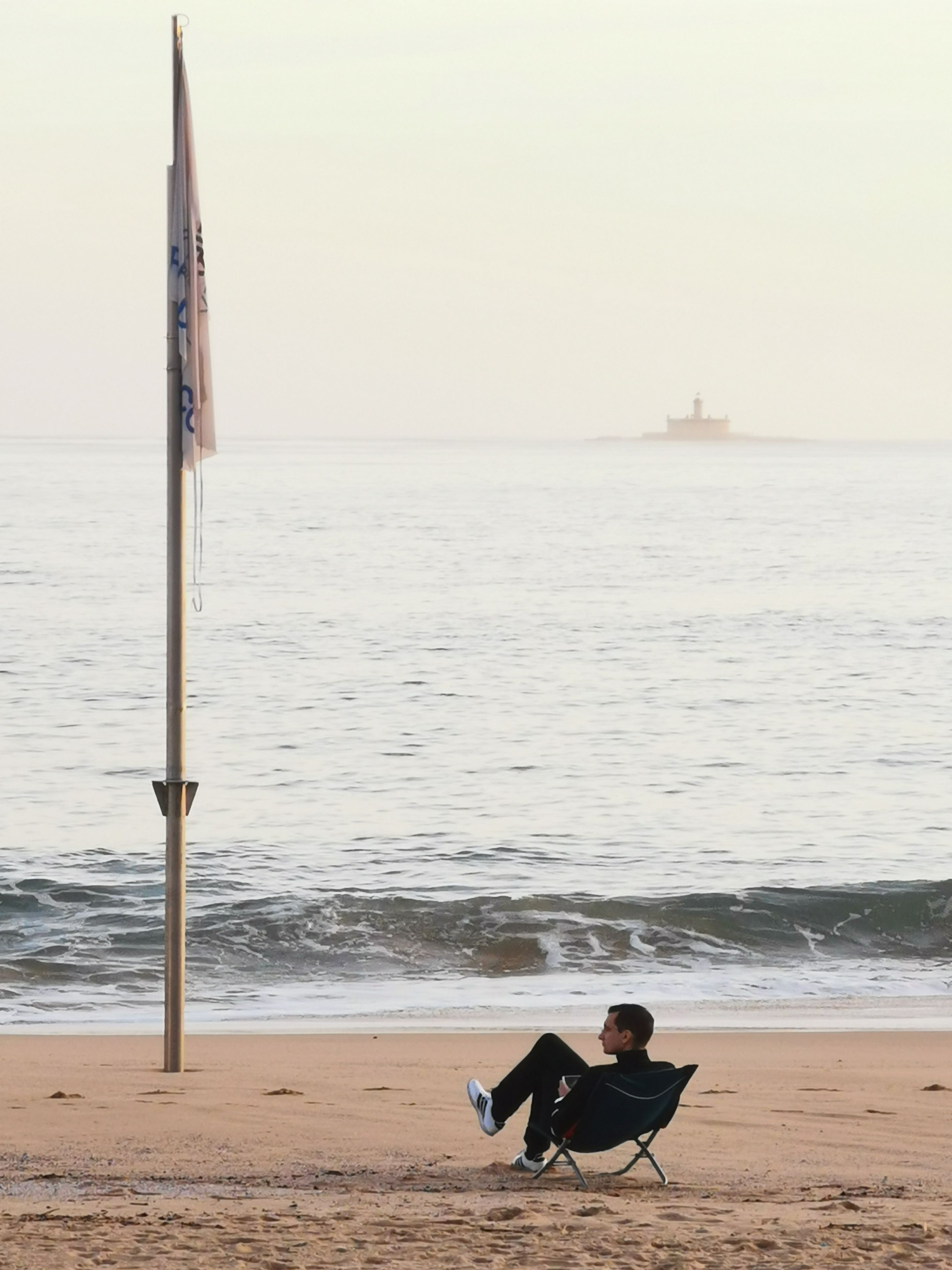 A man sitting on a chair by the serene beach, enjoying a peaceful sunrise