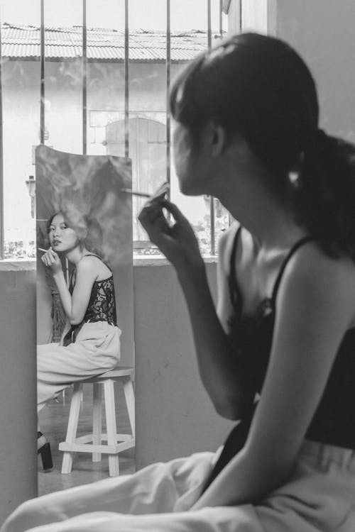 Free Woman Looking at Herself on a Full Size Mirror while Smoking Cigarette Stock Photo