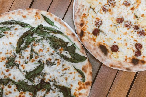 Two blistered pizzas with greens and melted cheese on a wooden table — photo by Roman Odintsov on Pexels