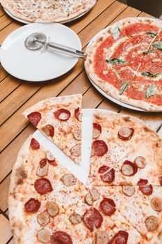 Assorted pizzas with pepperoni and sausage slices on a wooden table, ideal for food lovers.