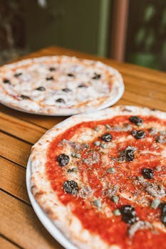 Close-up of Italian pizzas with olives on a wooden table, perfect for food photography.