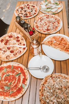 Top view of different pizzas with toppings displayed on a wooden table with a pizza cutter.