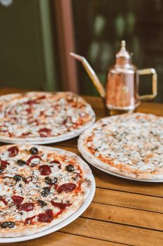 Three savory pizzas and a copper kettle on a wooden table for a tasty treat.