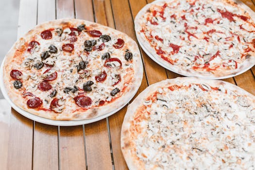 Close-up of assorted pizzas with mushrooms, pepperoni, and olives on a wooden table.