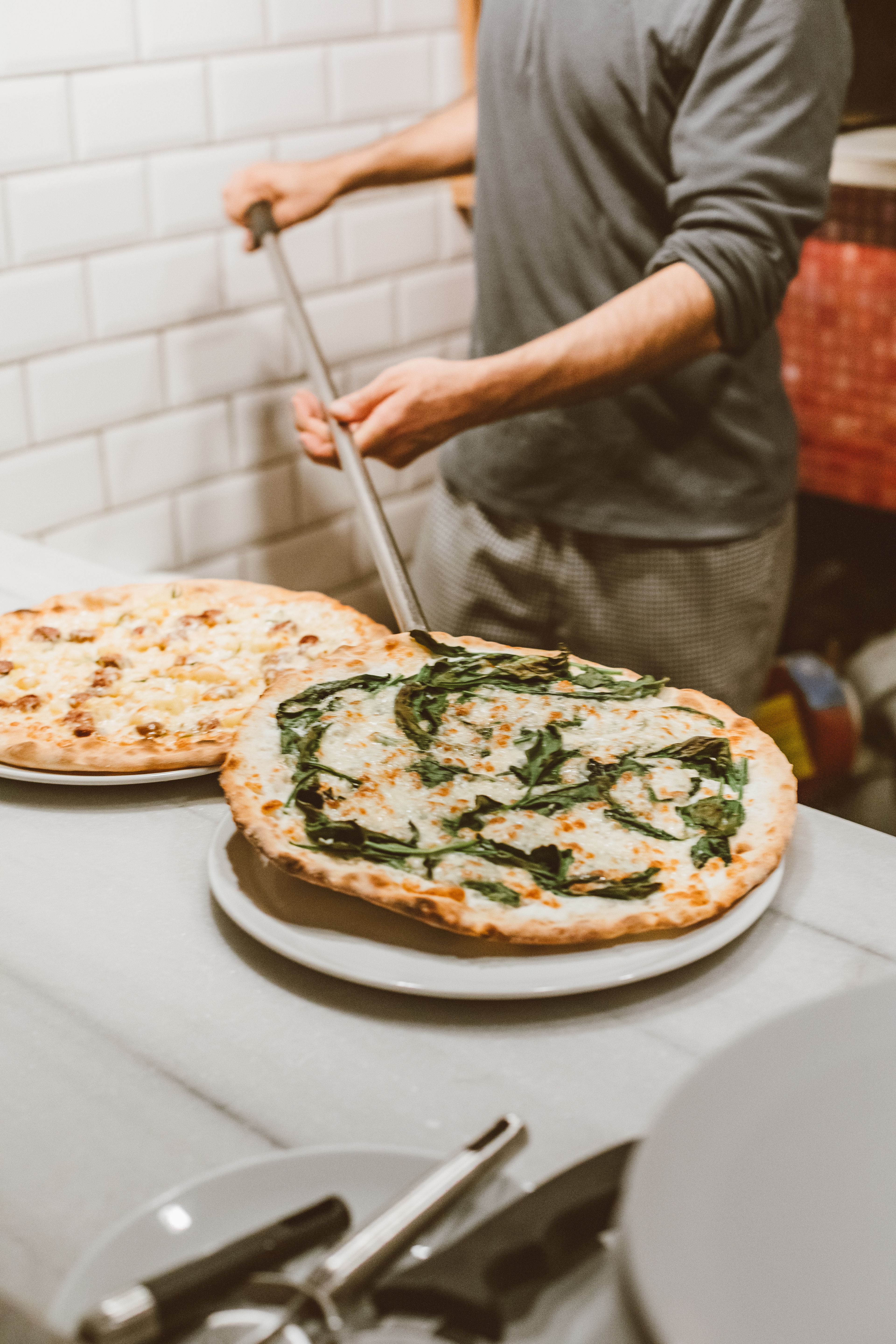 Pizzaiolo enfournant une pizza dans un four traditionnel, dont le conduit est distinct de celui de la hotte