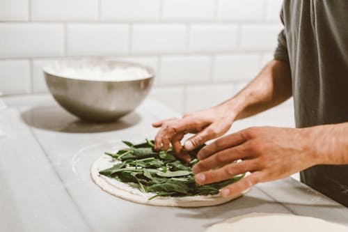 A Person Putting Vegetables Topping on a Dough