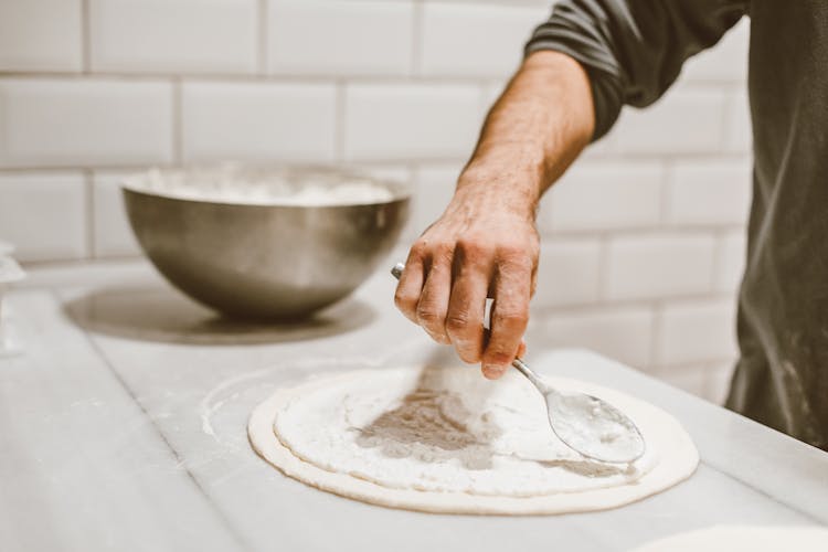 A Person Spreading The Sauce On A Dough