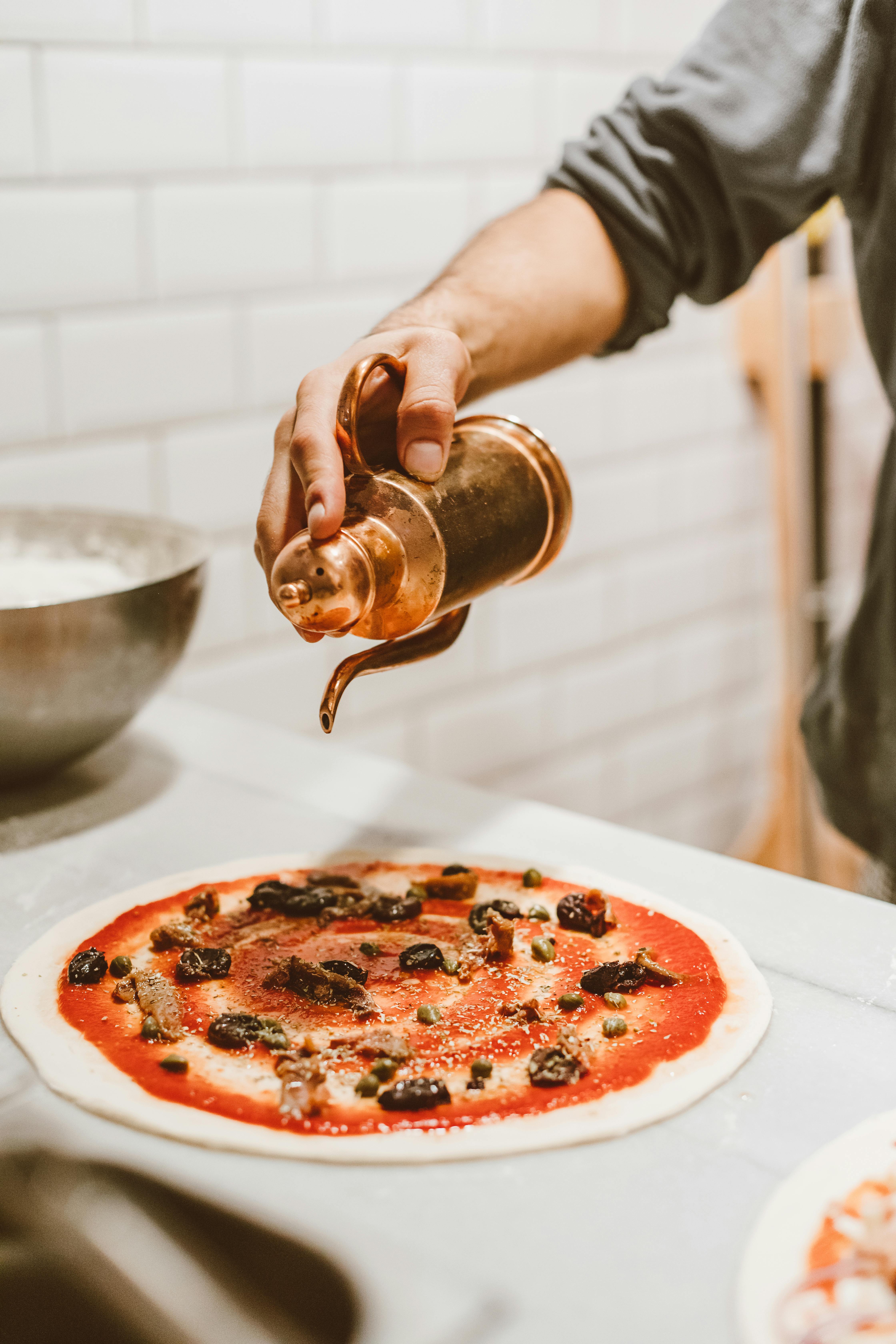 cook pouring olive oil on pizza dough