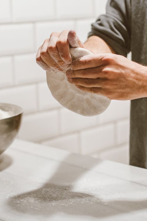 Free Close-up of hands kneading dough on a marble countertop in an indoor kitchen setting. Stock Photo