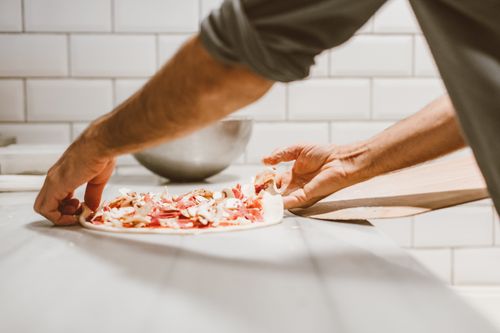 Free A detailed view of hands adding toppings to a pizza in a kitchen setting. Stock Photo