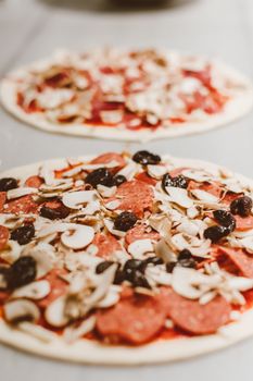 Close-up of uncooked pepperoni pizzas with olives and mushrooms, ready to bake.