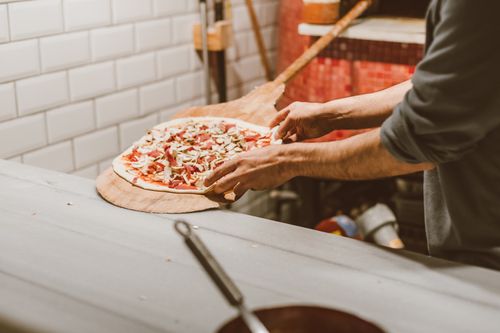 Free Close-up of hands placing a pizza in a brick oven in a rustic kitchen. Stock Photo