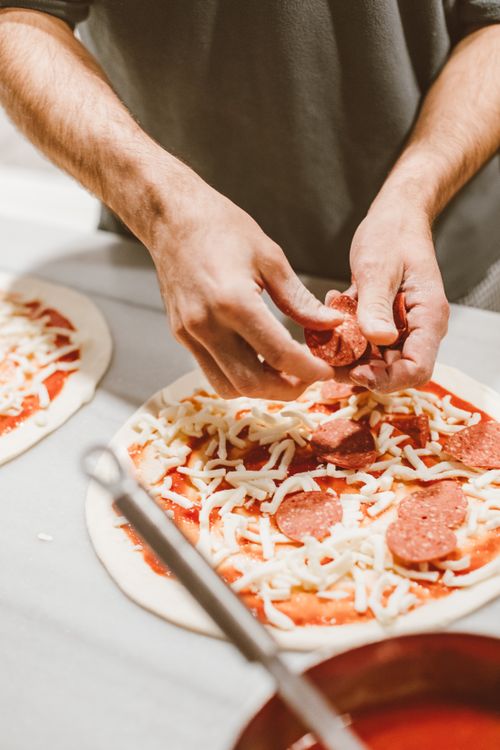 Free Close-up of hands placing pepperoni slices on a pizza with cheese and tomato sauce. Stock Photo