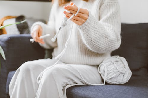 Woman in White Sweater Sitting on the Couch while Knitting
