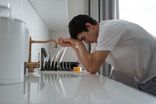 A young man appears tired and stressed, leaning on a kitchen counter in contemplation.