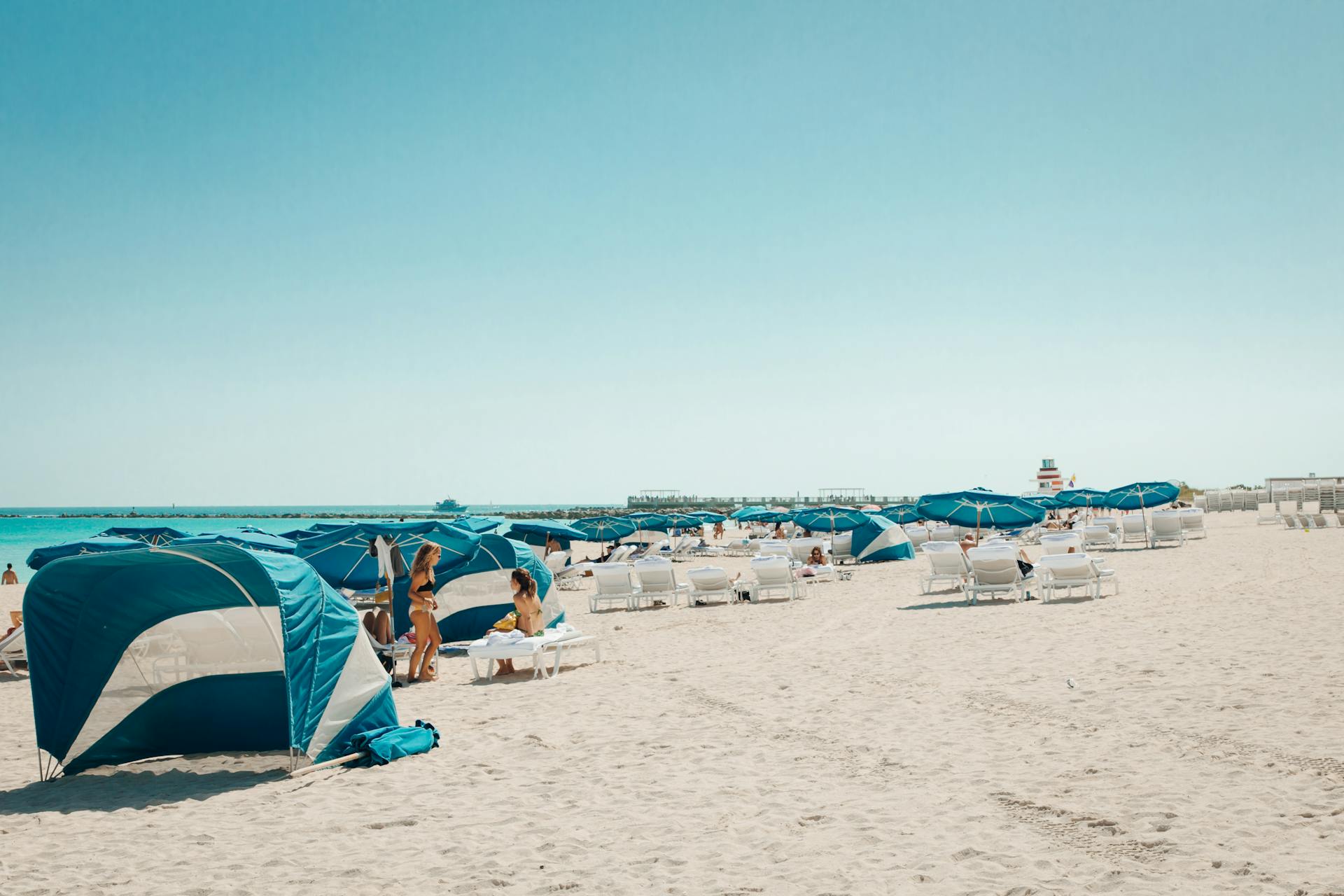 Relaxing scene at Miami Beach with blue umbrellas and people enjoying a sunny day.