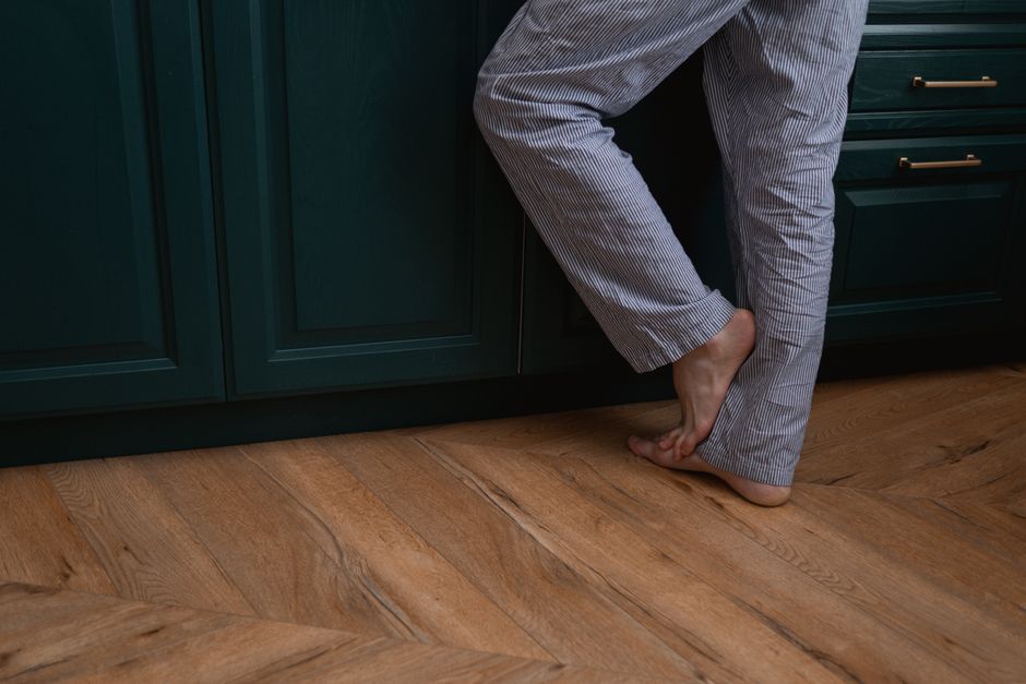 Person standing barefoot in striped pajamas on a wooden floor by green cabinets.