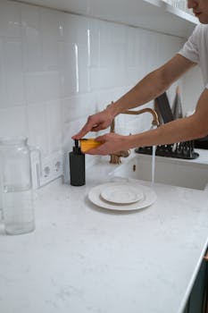 Close-up of hands washing dishes at a modern kitchen sink with white counter.