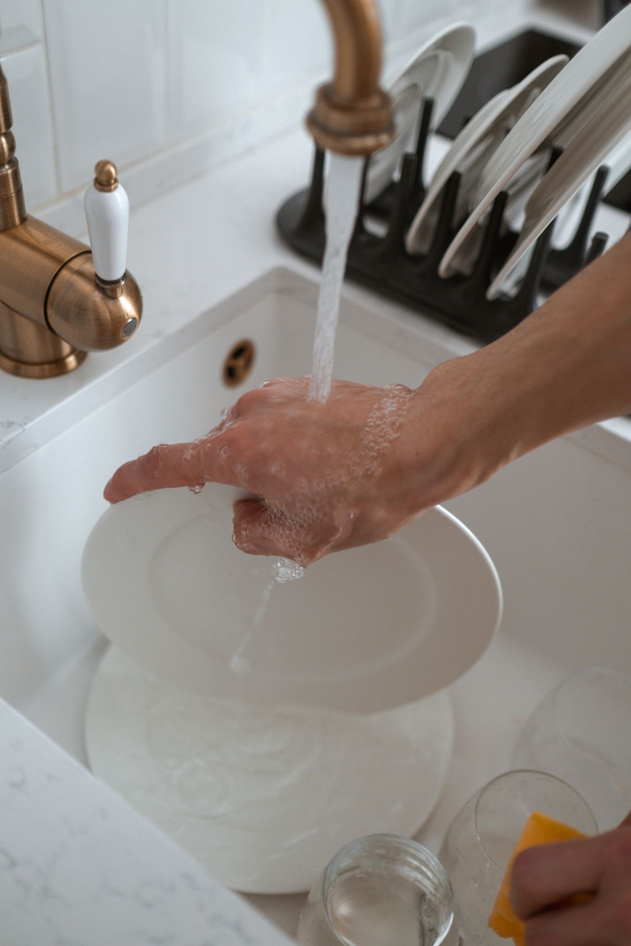 Hands washing dishes under a brass faucet