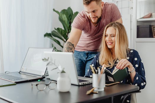 Two professionals collaborating at a desk with laptops in a bright, modern office.