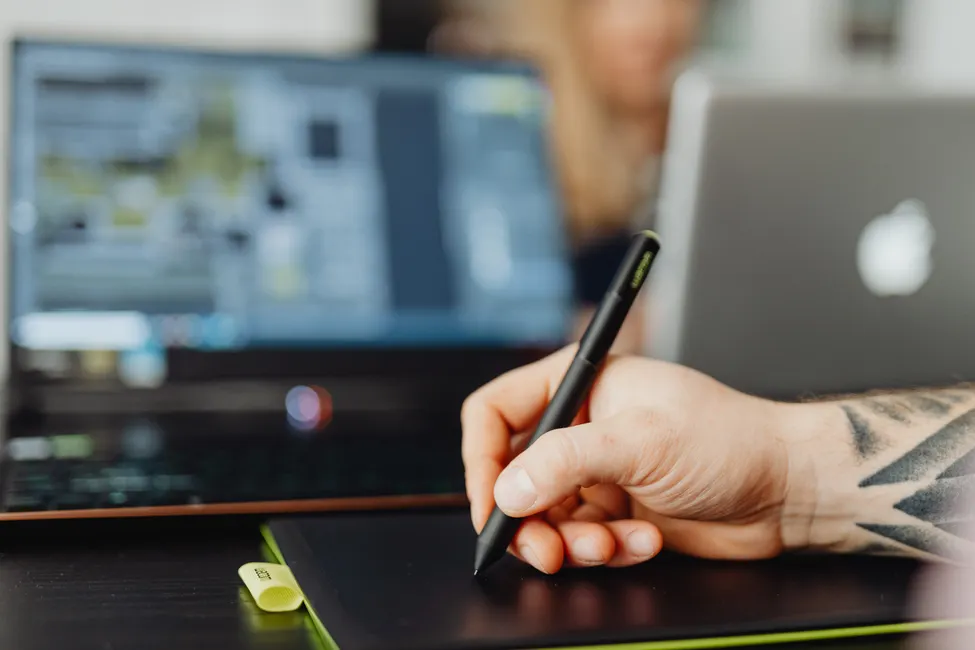 Main utilisant un stylet sur une tablette graphique devant un écran de mise en page