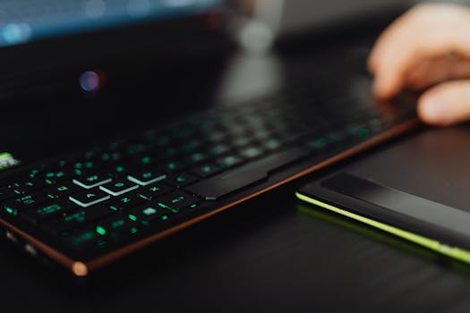 A close-up of a backlit gaming keyboard and laptop, highlighting modern technology use.