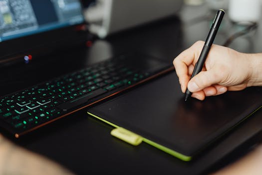 Close-up of a hand using a stylus pen on a graphic tablet at a modern workspace.