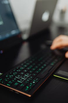 Close-up of a backlit keyboard with a person using a laptop in a blurred background.