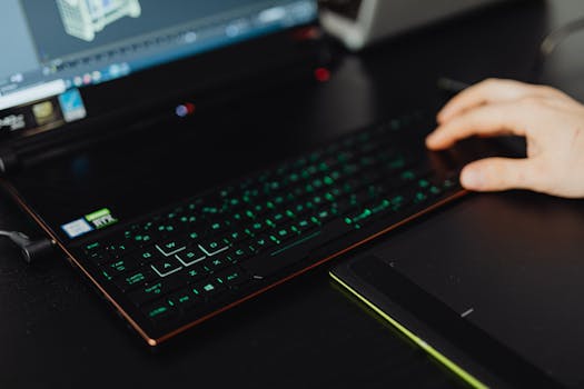 Close-up of a person working on a laptop with an illuminated keyboard at a desk.