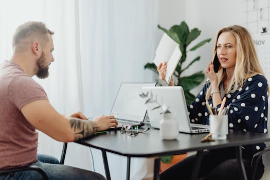 Business colleagues working at a desk using laptops and phones in a modern office setting.