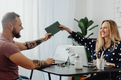 Man and Woman Holding Notebook while Sitting at the Table