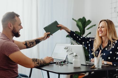 Free Two happy coworkers sharing ideas at a desk with laptops, indoors. Stock Photo