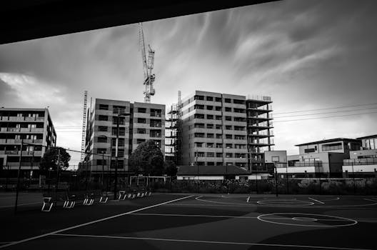 Grayscale view of an empty basketball court against a backdrop of modern buildings under construction.