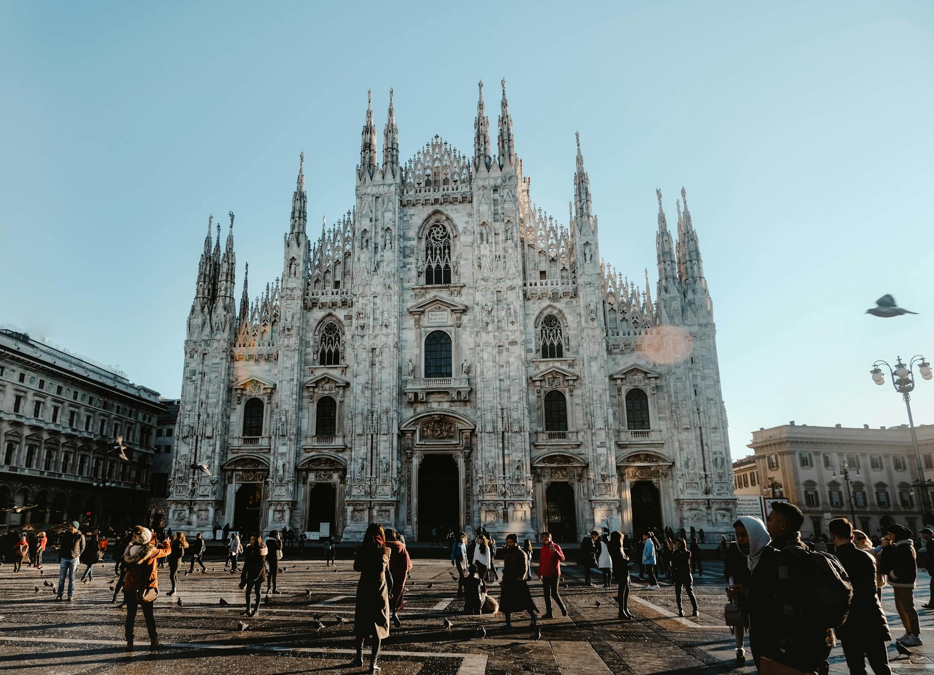 Capture of the iconic Duomo di Milano with bustling tourists under clear skies.