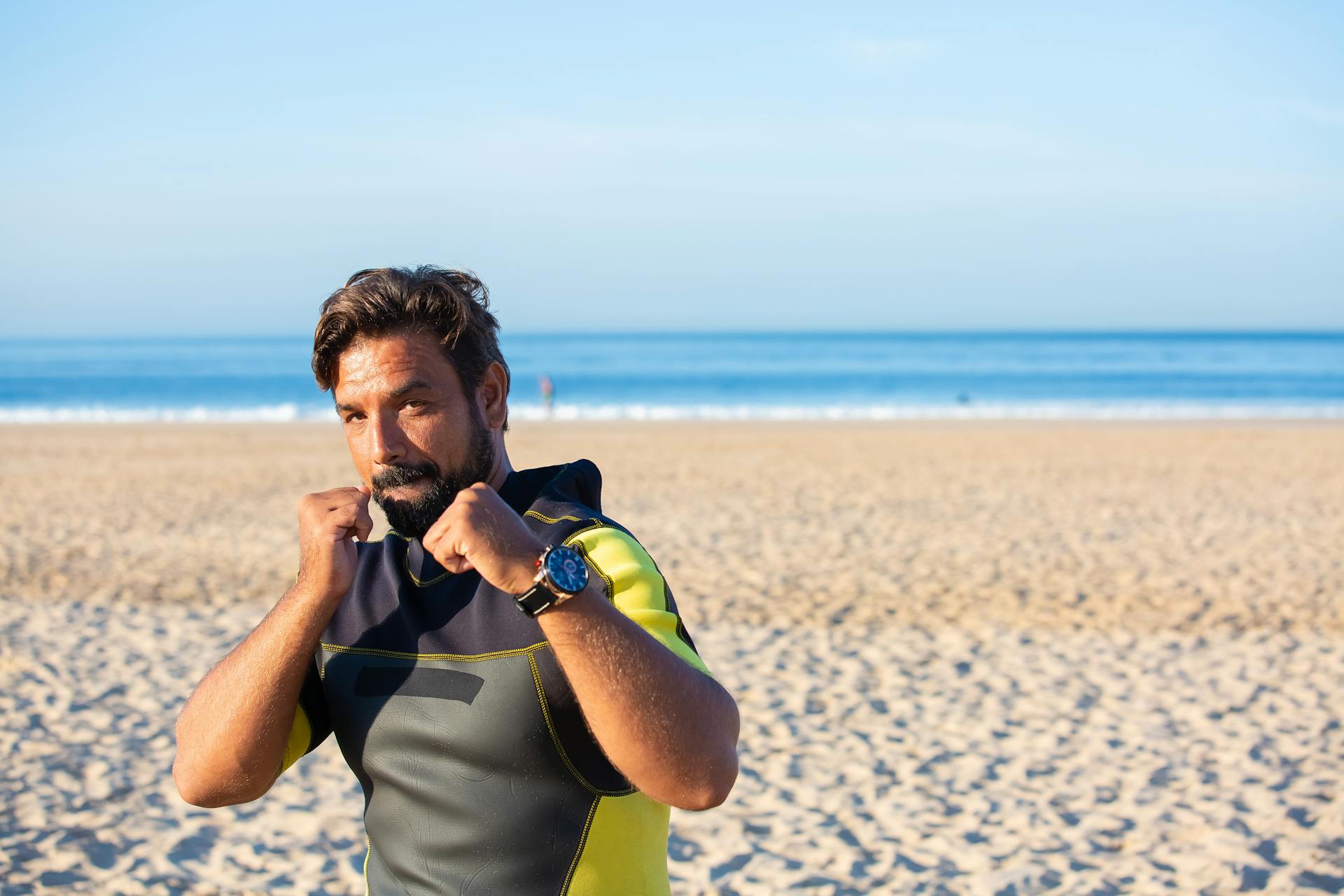 Concentrated male looking at camera holding clenched fists while shadow boxing on sandy beach