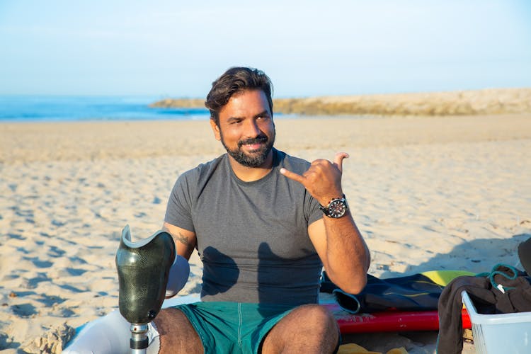 Tanned Disabled Man Showing Shaka Sitting On Beach