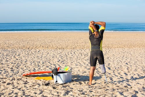 Free Faceless amputee man stretching body on beach before surfing Stock Photo