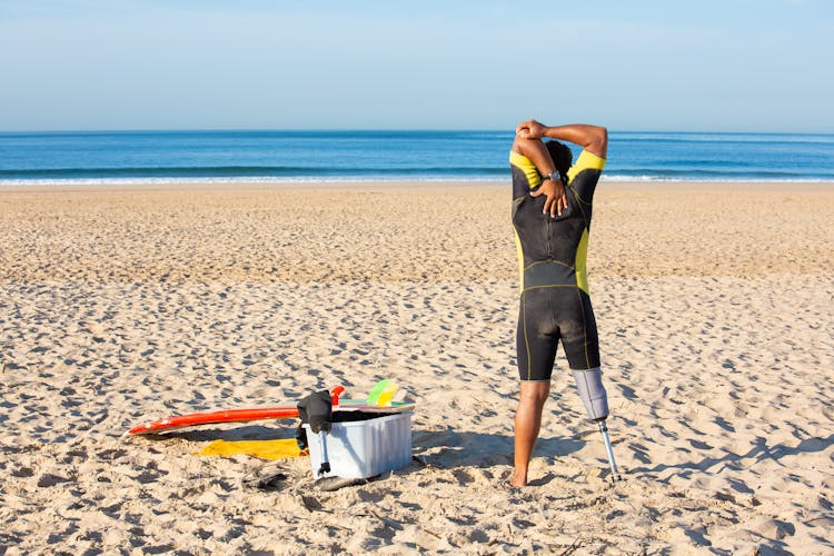 Faceless Amputee Man Stretching Body On Beach Before Surfing