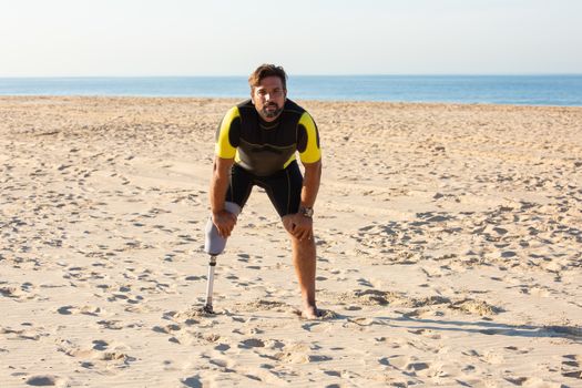 Ethnic amputee man standing on beach with hands on knees