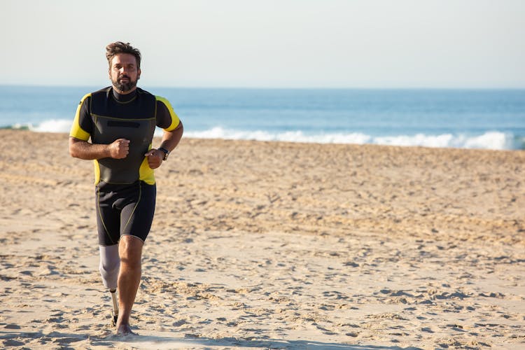 Dedicated Ethnic Sportsman Amputee Jogging On Sandy Coastline