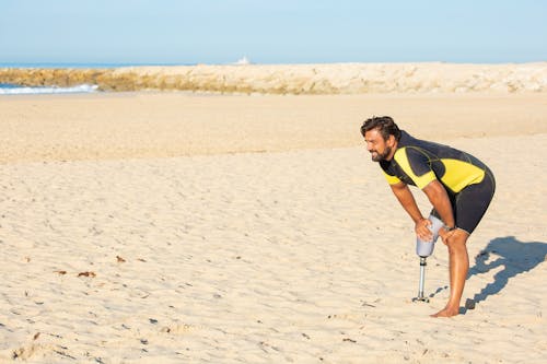 累了的運動員截肢者，手放在海灘上的膝蓋上休息
