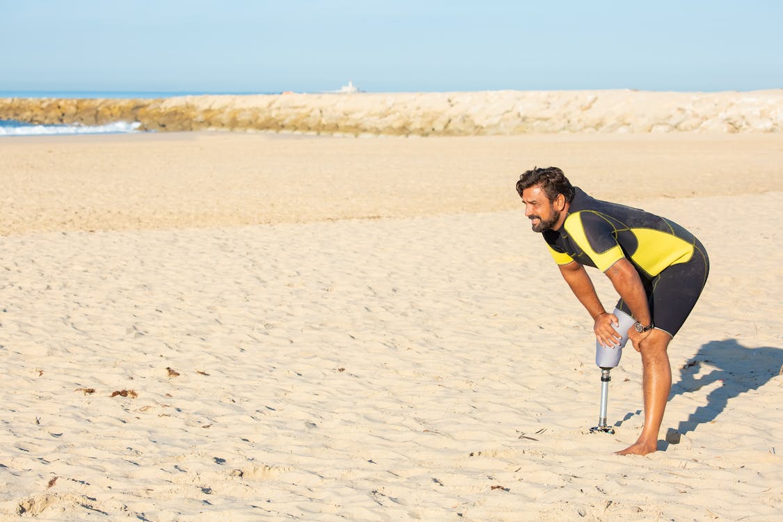 Tired sportsman amputee resting with hands on knees on beach