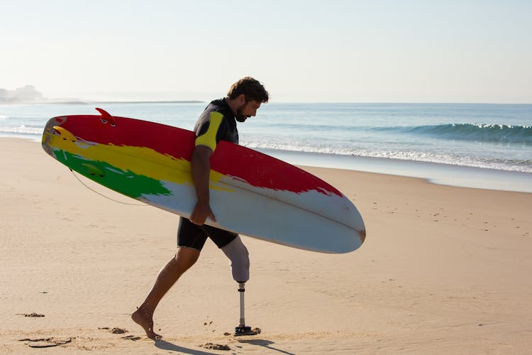 Amputee Man Surfer With Surfboard Walking Towards Waving Sea