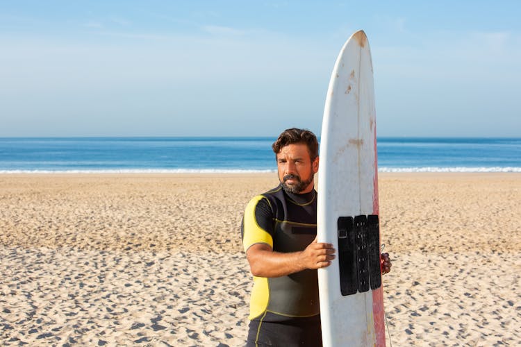 Fit Ethnic Male Surfer With Surfboard Standing On Beach