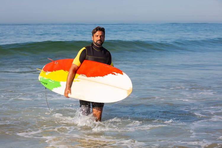 Confident Ethnic Male Surfer Walking In Sea Waves